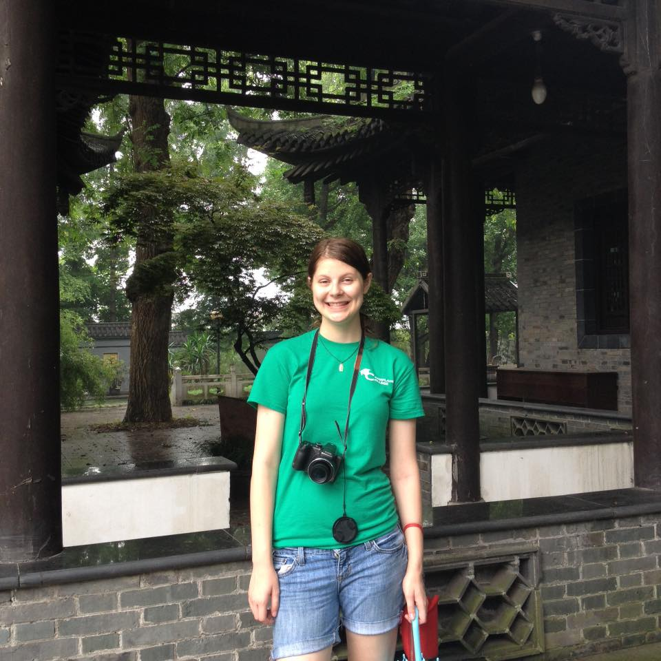 College student in green shirt with camera, outside a shrine and garden at YangZhou Social Welfare Institute, an orphanage in Shanghai, China. Today, she is studying Mandarin Chinese at Capital Region Language Center.