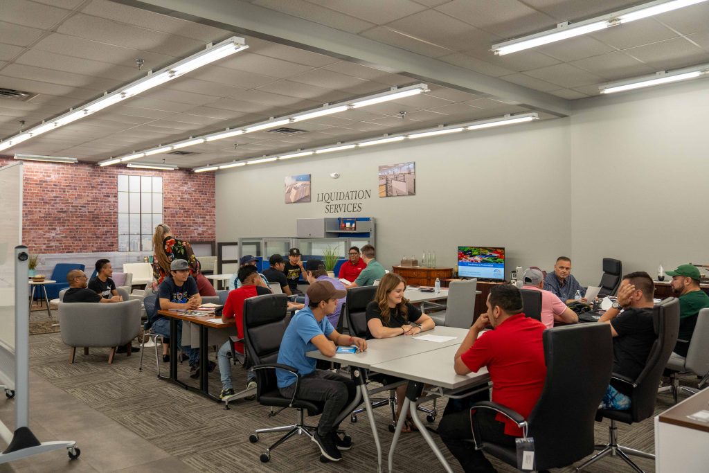 Turnkey employees listen to CRLC's Kim Andersen, during an after-work English class, offered in the company's Troy showroom. Group is seated at tables, with Andersen at the head of the room, speaking to the group.