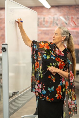 Kim Andersen, founder and director of Capital Region Language Center, teaches an English lesson at Turnkey Workplace Services. Andersen is standing and writing on a white board in the company's showroom.