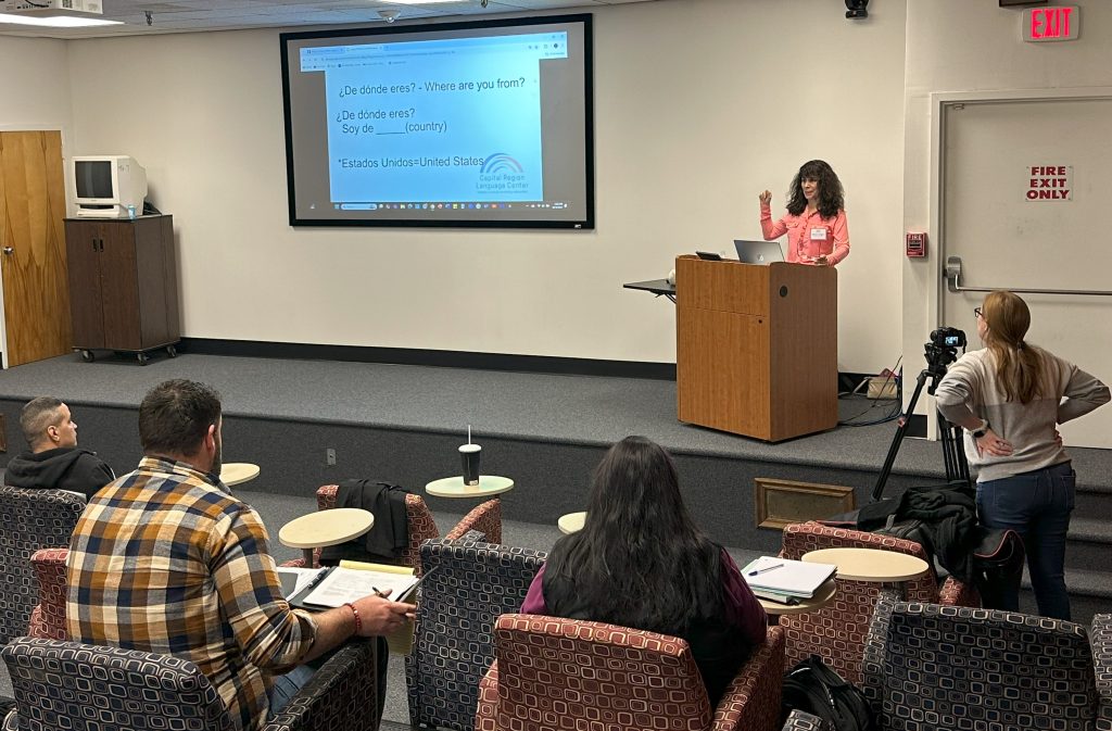 Teacher at podium, instructing distribution center supervisors at Market32 / Price Chopper in Spanish, using projection screen.