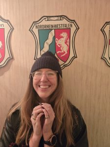 Woman in glasses and black beanie hat, beneath German crest at Albany German American Club 